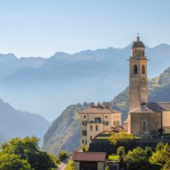 Historisch bergdorp in Graubünden met kerktoren en Alpen op de achtergrond
